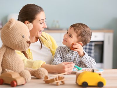 Picture of a Live-In Nanny feeding cute young boy with his teddy bear in the kitchen